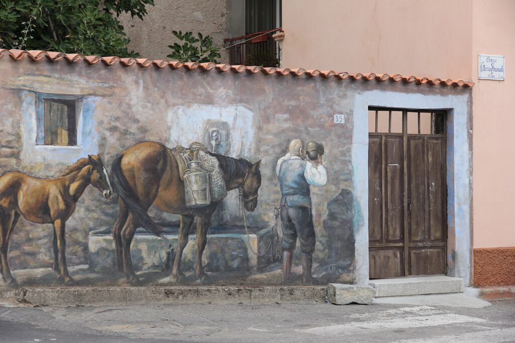 Murale con un cavallo e un uomo alla fontana su una casa di Fonni