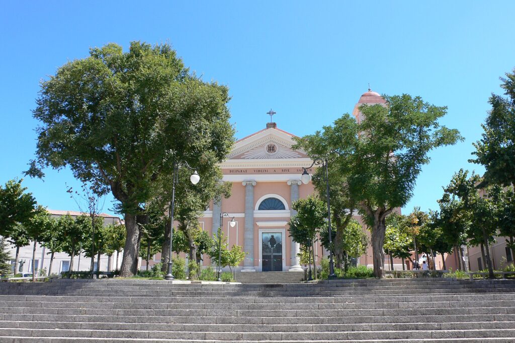 Facciata della cattedrale di Santa Maria della Neve a Nuoro tra gli alberi della piazza